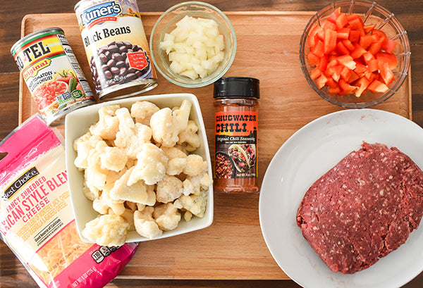 ingredients for taco cauliflower bake, ground beef, diced red bell pepper, frozen cauliflower, black beans, diced tomatoes with green chilies, shredded cheese, onion, and chugwater chili seasoning