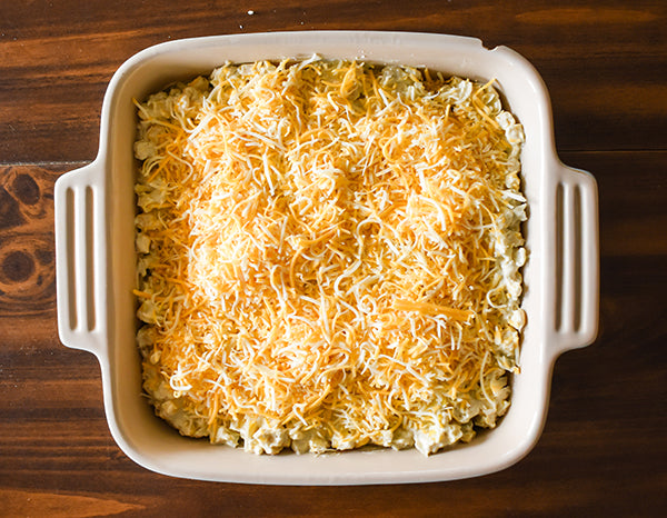 creamy green chili corn bake in baking dish with shredded cheese on top ready to be baked