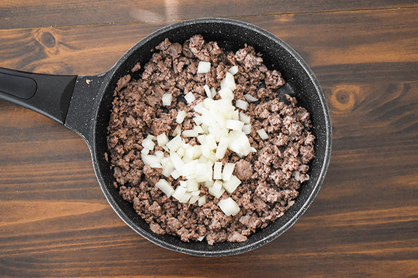 browned ground beef with diced onion in frying pan