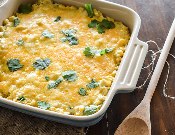 cooked creamy green chile bake in baking dish with wooden spoon beside it