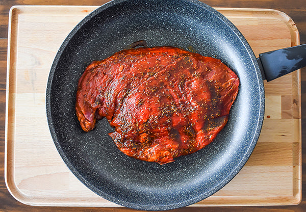 chugwater chili steak rub marinated Flank Steak in a skillet ready to be cooked