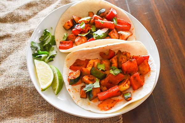 baked vegetable tacos on plate with cilantro garnish and lime wedges