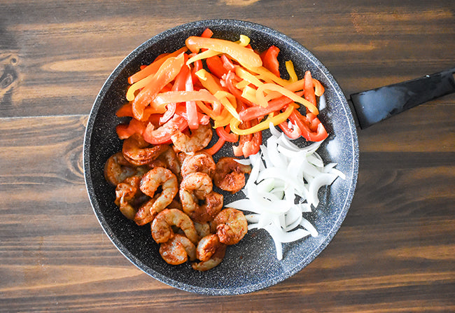 peppers, onion, and shrimp in skillet with olive oil