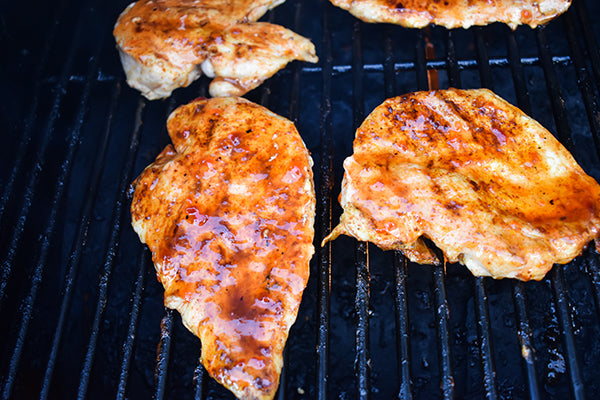 Chugwater Chili red pepper jelly added to chicken breasts on grill