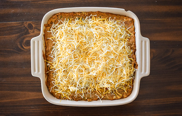 shredded fiesta cheese added to the top of the partially baked bean dip in baking dish