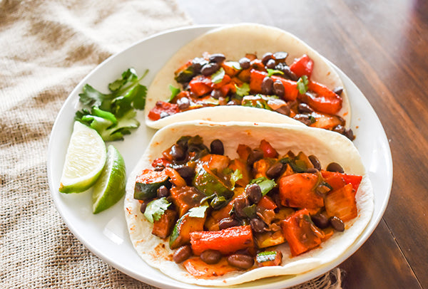 seasoned black beans added to baked vegetable taco on plate with cilantro garnish and lime wedges