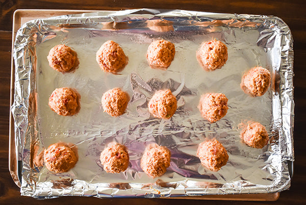 spicy crema cheese sausage balls on baking sheet that has been lined with foil and sprayed with cooking spray