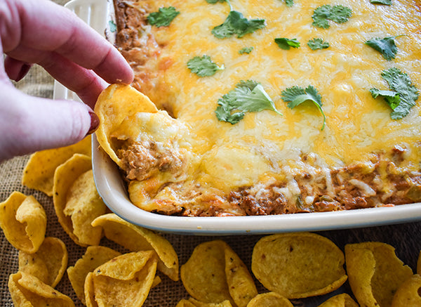 creamy fiesta bean dip in baking dish ready to serve with corn chip scoops