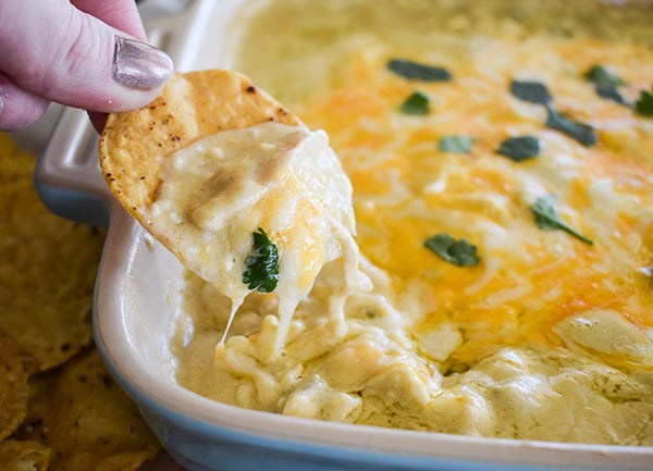 green chile chicken enchilada party dip scooped up with tortilla chip