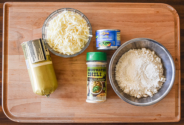 ingredients for cheesy green chile sausage balls on cutting board, pork sausage, shredded monterey cheese, diced green chilies, bisquick, and chugwater chili green chili seasoning