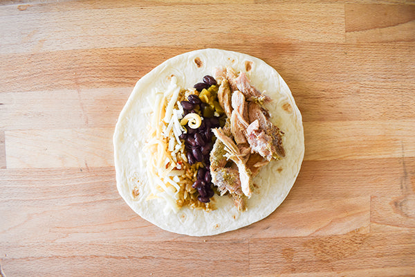 tortilla shell with rice, black beans, diced green chilies, seasoned chicken, and shredded cheese ready to be rolled and placed in baking dish