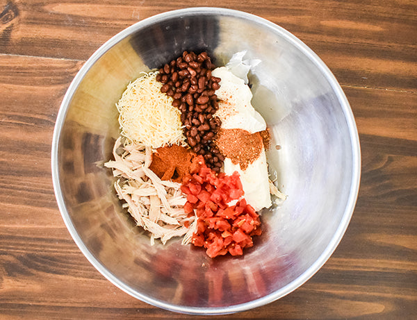 ingredients for roll up filling in bowl shredded chicken, shredded cheese, diced tomatoes with green chilies, black beans, chugwater chili seasoning, chugwater chili dip mix, sour cream