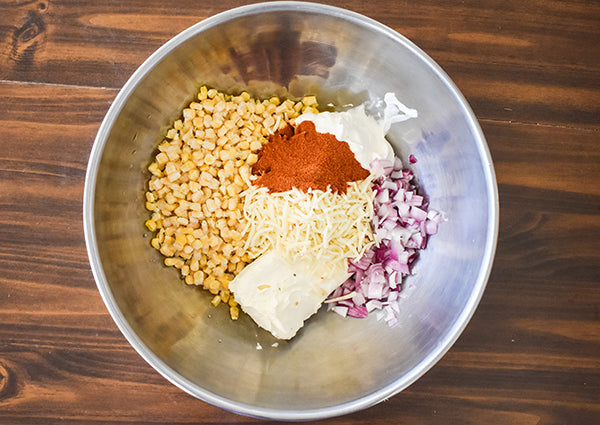 ingredients for street corn dip in bowl ready to be mixed, whole kernel corn, softened cream cheese, sour cream, red onion, pepper jack cheese, and chugwater chili seasoning