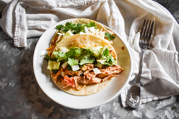 shredded chicken tacos in corn tortillas with lettuce and onion toppings on tray on plate with cilantro and onion