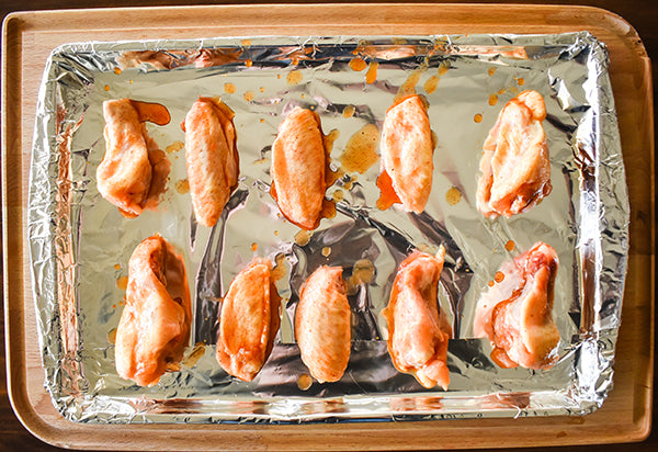 Chili pineapple sauce covered chicken wings on cookie sheet ready to be baked