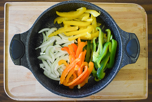 Sliced bell peppers and onion in skillet with oil