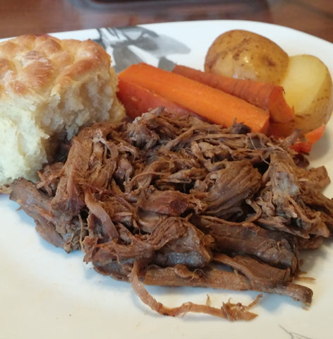 up close photo of roast, potatoes, carrots, and roll on plate