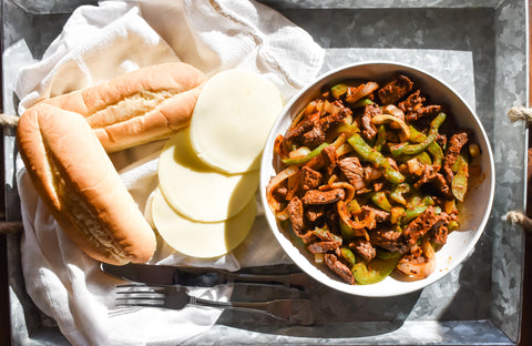 Photo of philly cheesesteak filling, buns, and cheese on a tray