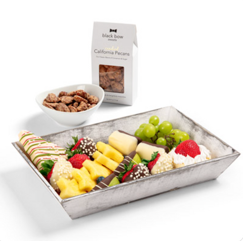 Image shows Edible Arrangements dessert board with fresh and chocolate dipped fruit next to box and bowl of Black Bow Sweets candied pecans