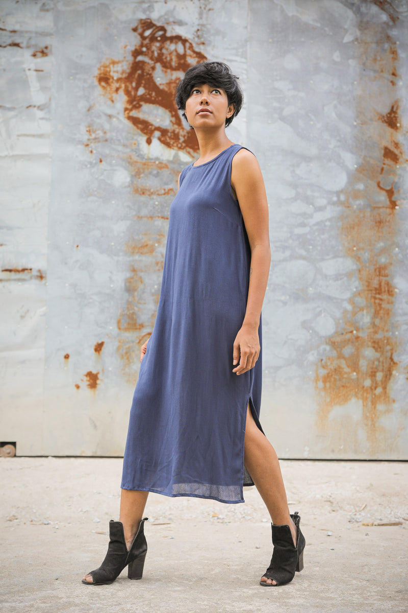A model shown taking a bold step in our zero waste navy blue cotton crepe sleeveless dress which cuts mid calf.   