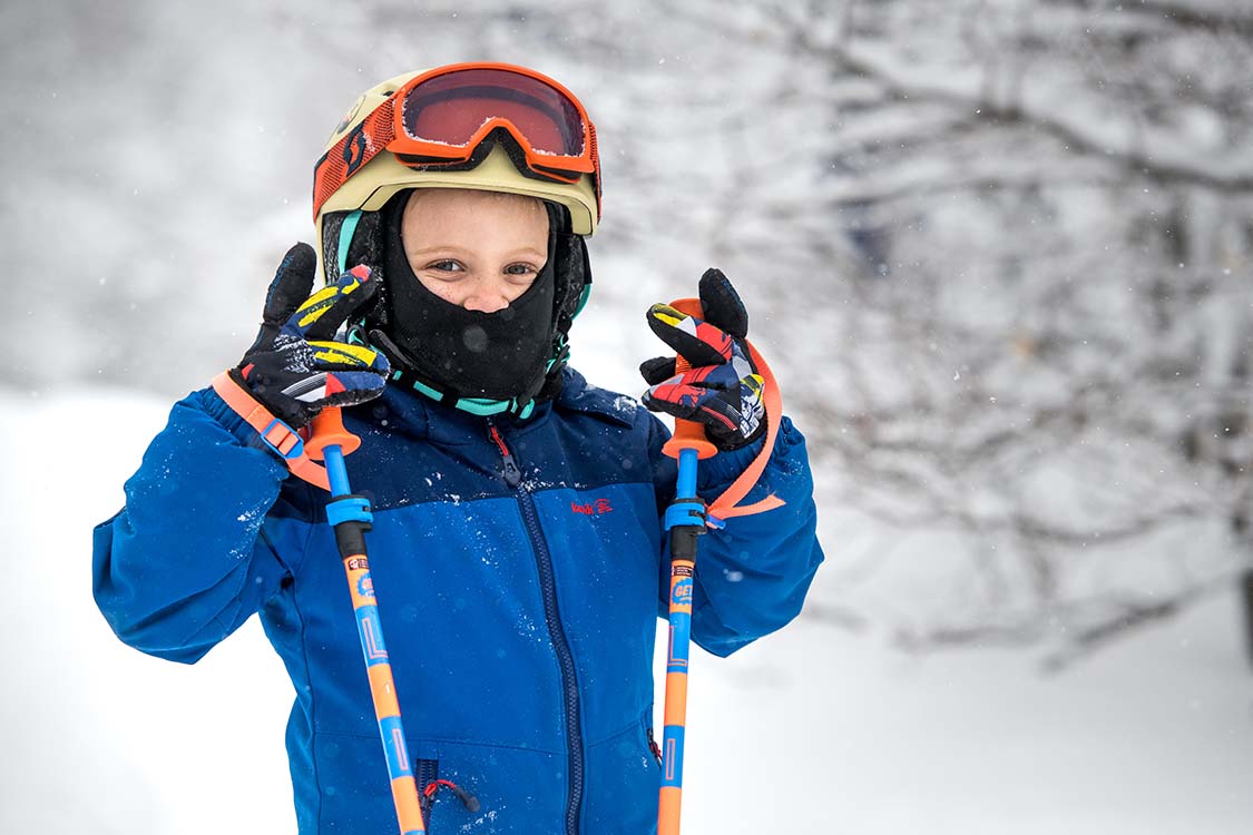 Child flashing peace signs holding ski poles