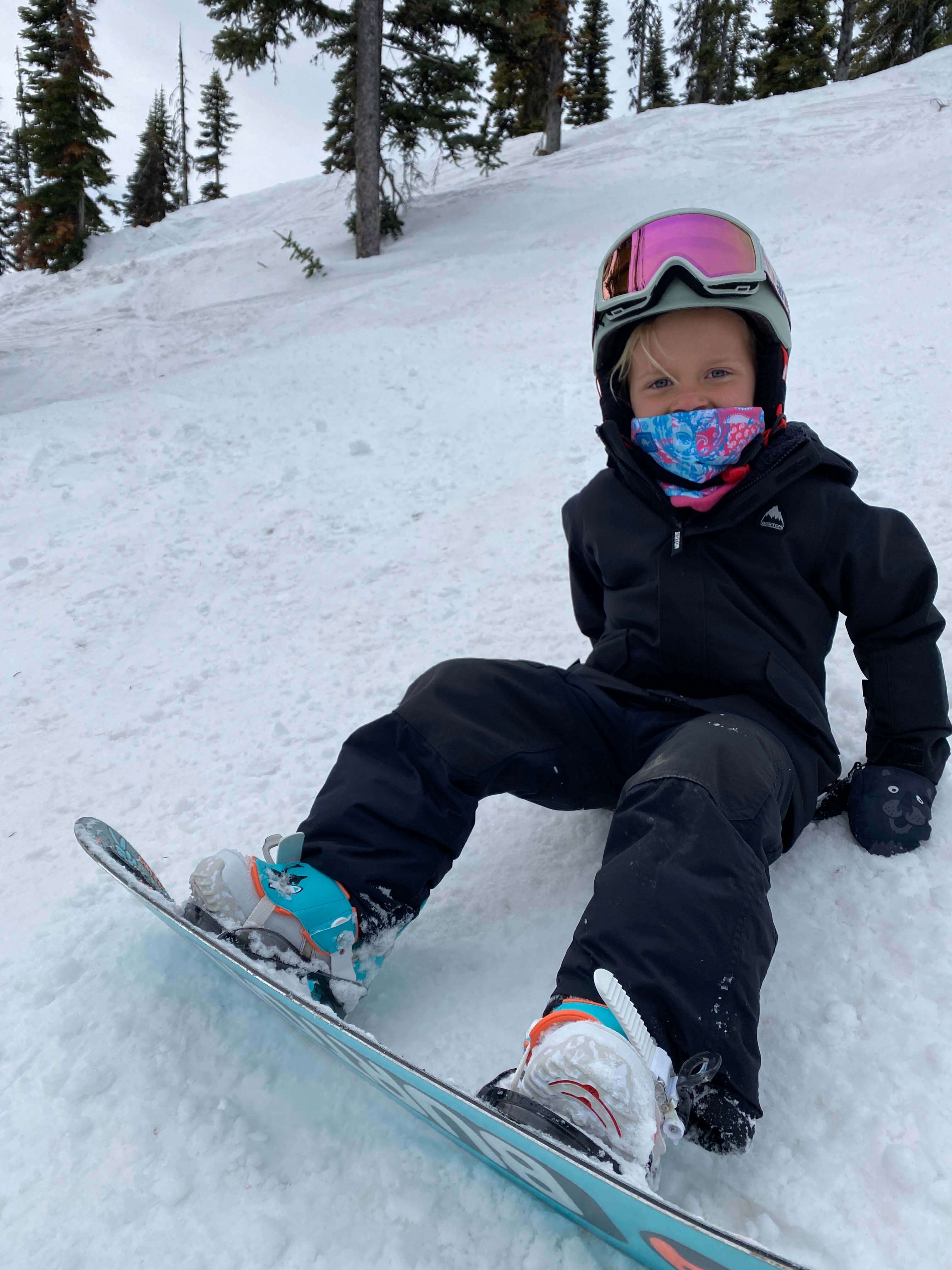 Kid sitting in snow wearing ski pants and jacket