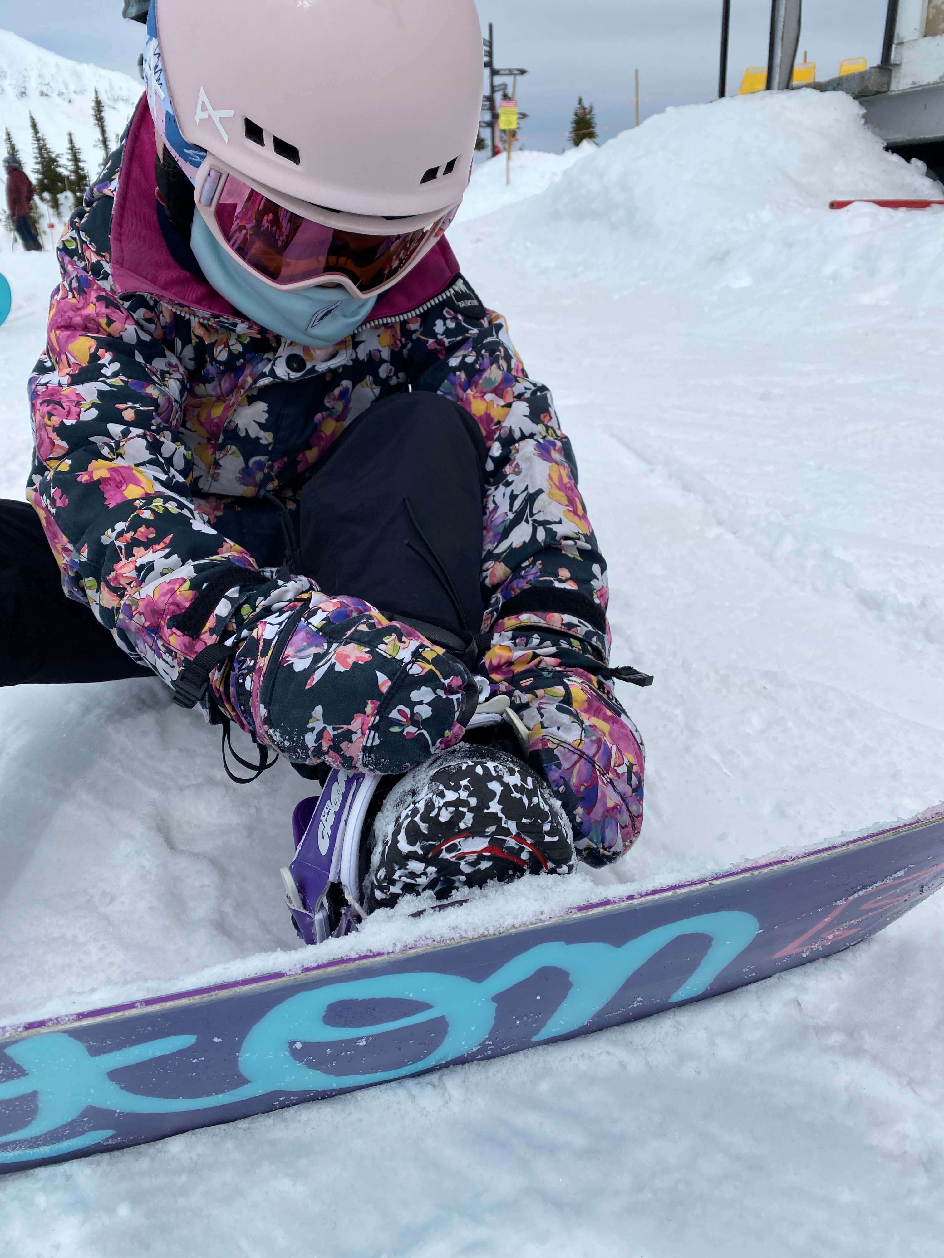 Child with gloves adjusting snowboard bindings