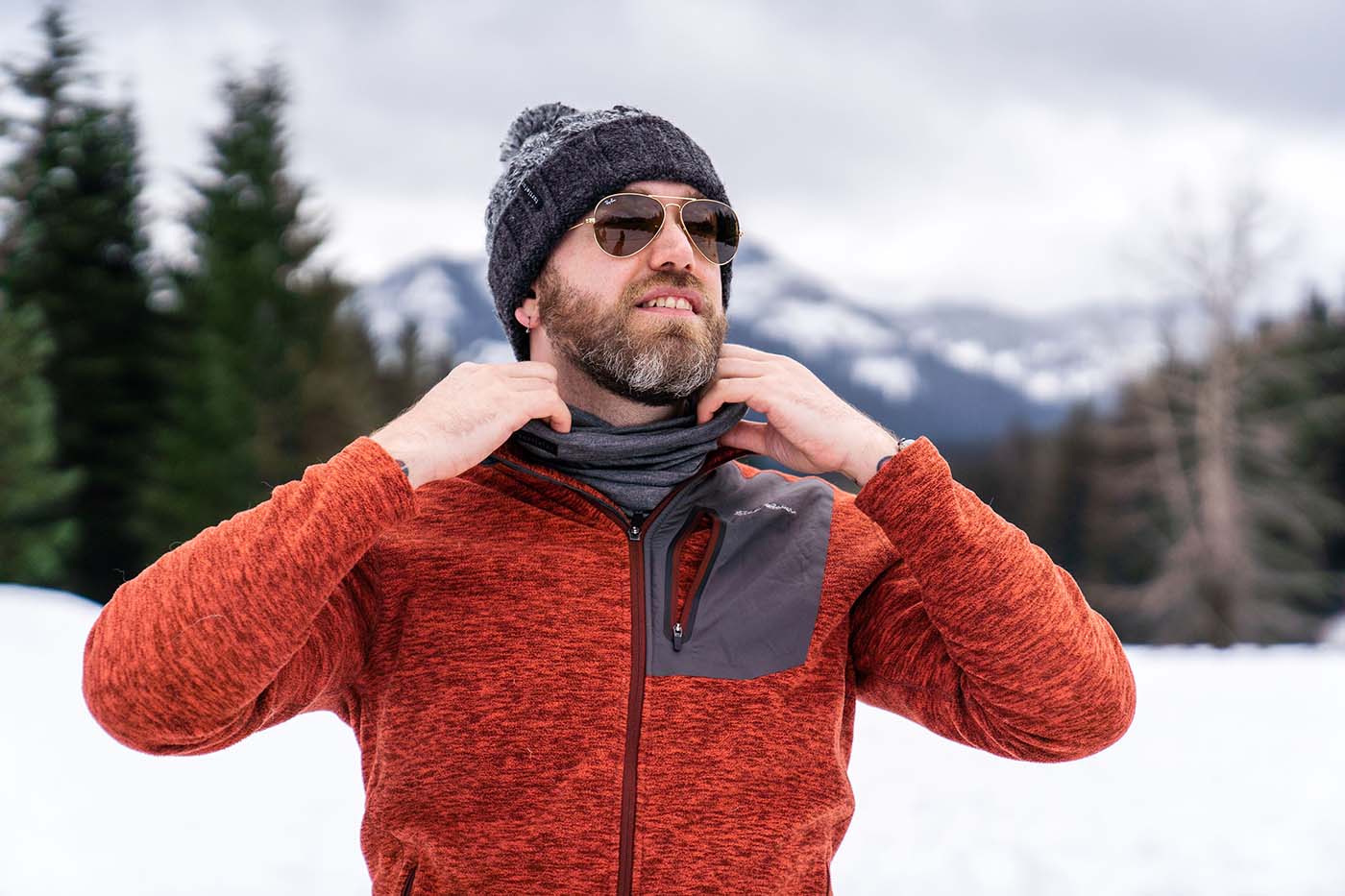 man adjusts neck gaiter in front of snowy background