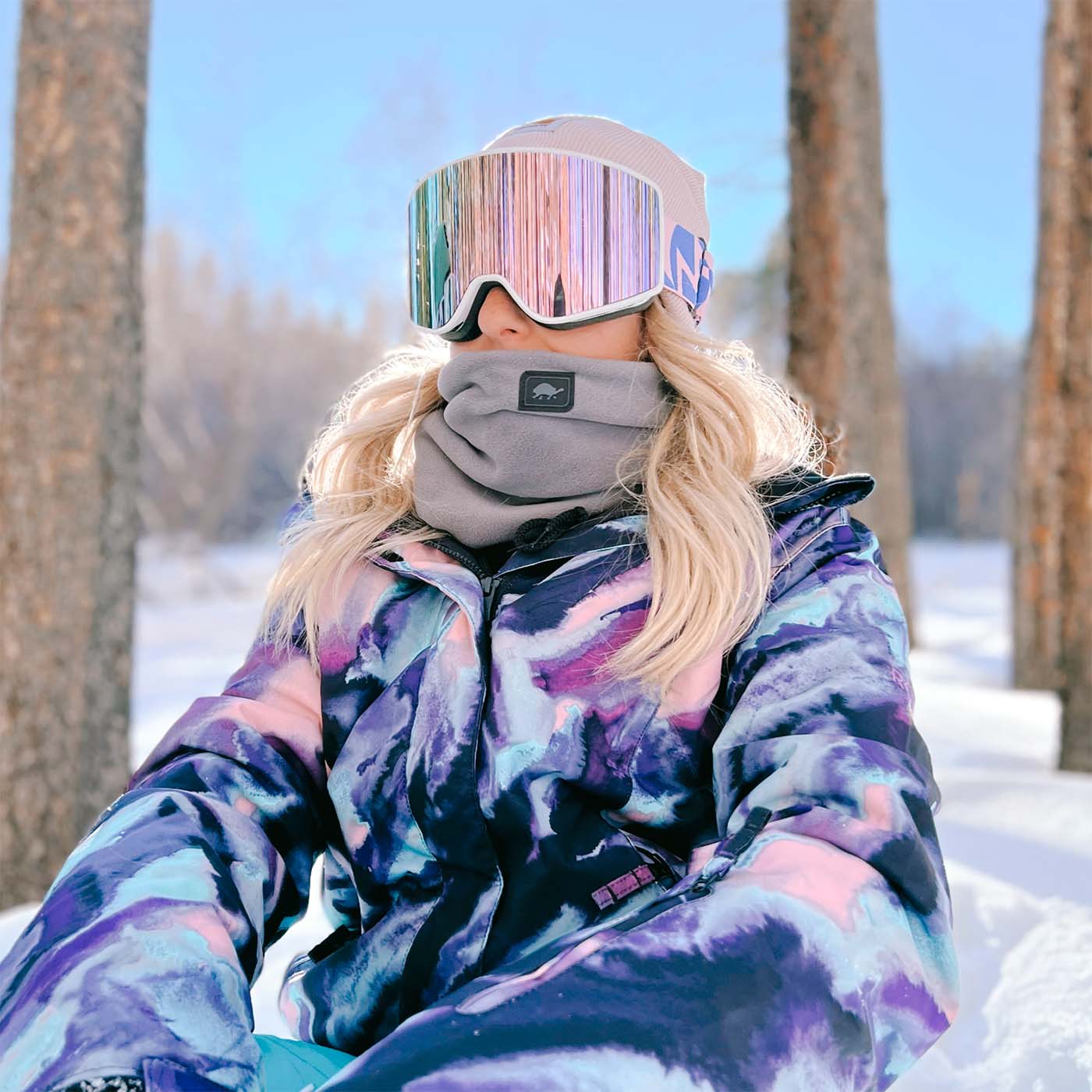 photo of girl sitting between trees wearing neck warmer and goggles