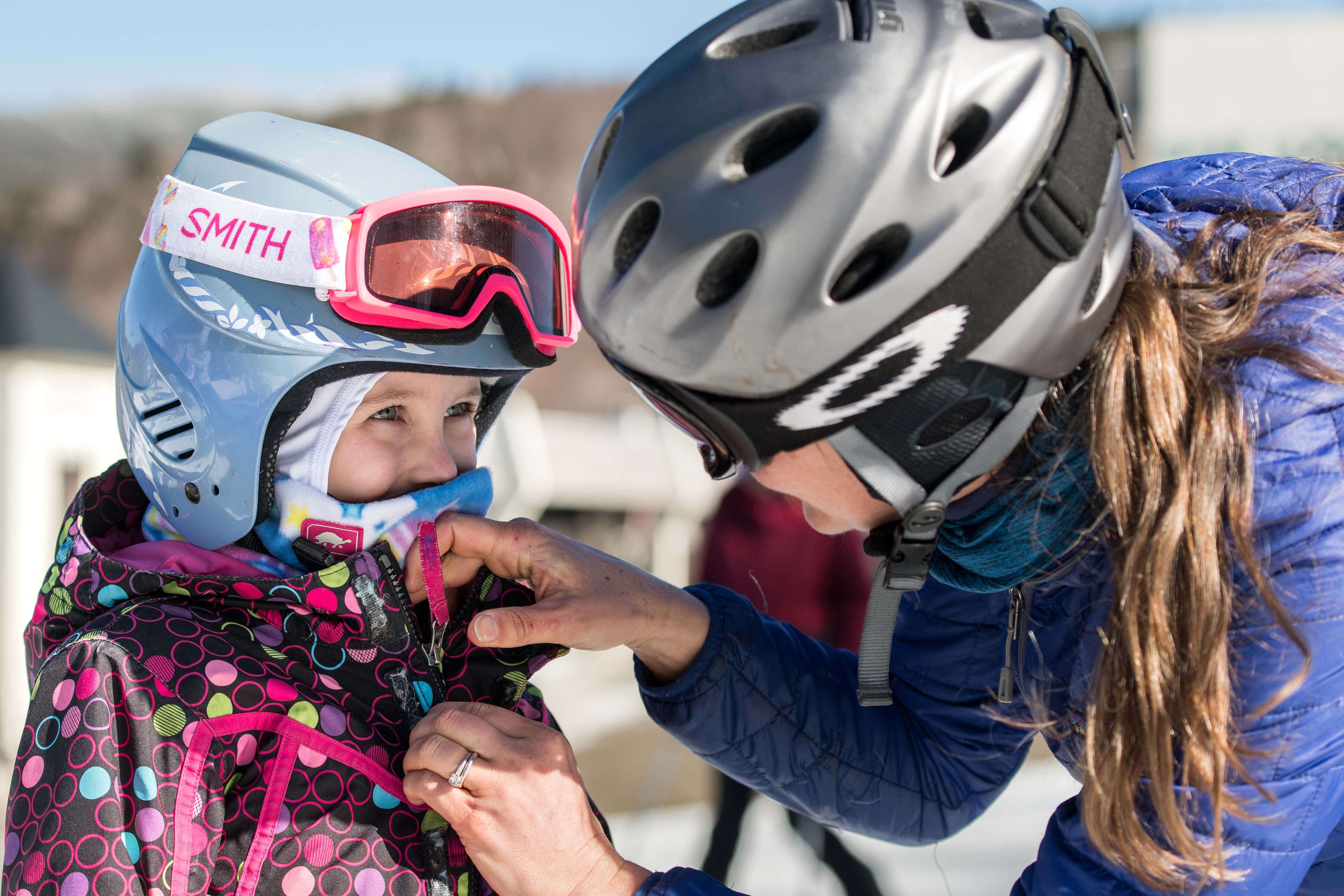 Mother adjusting child's balaclava and ski helmet