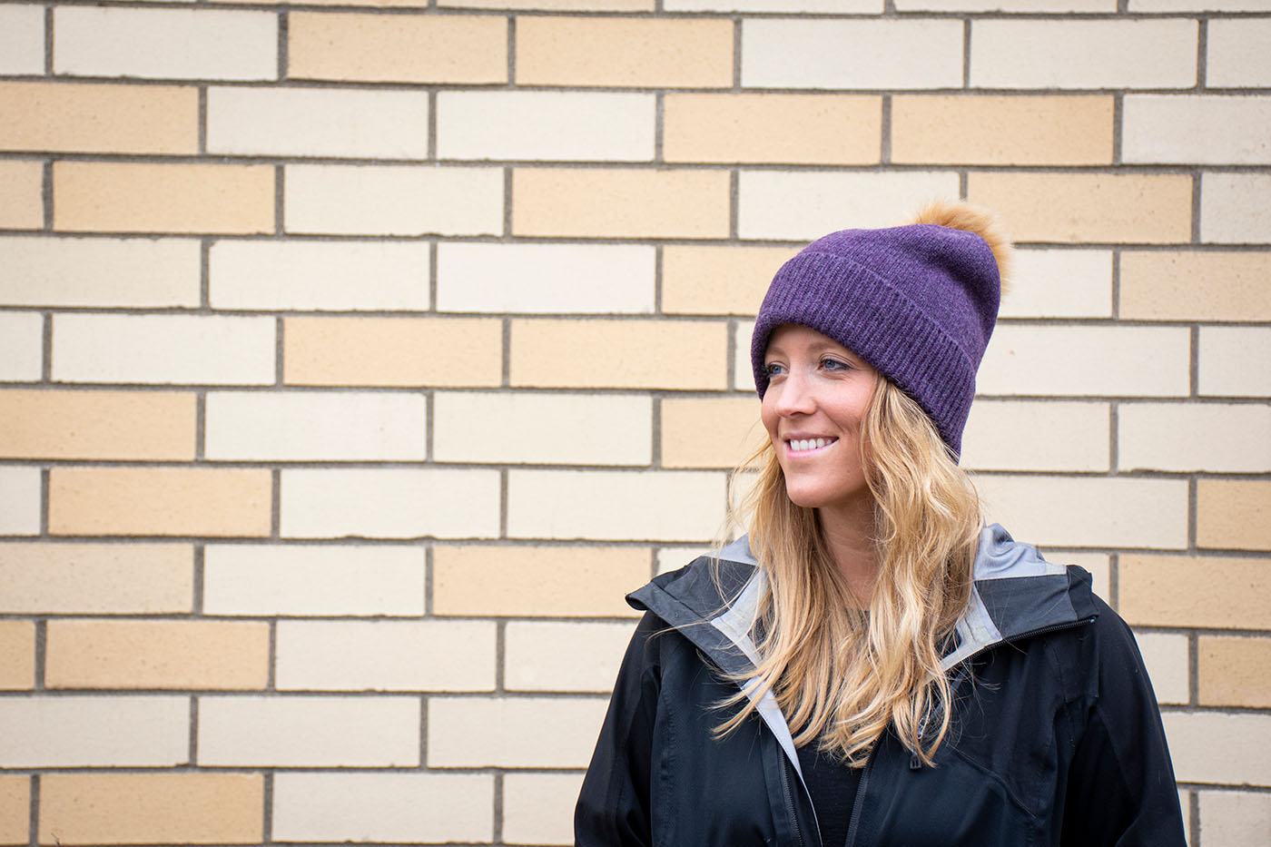 woman poses wearing pom beanie in front of tile wall