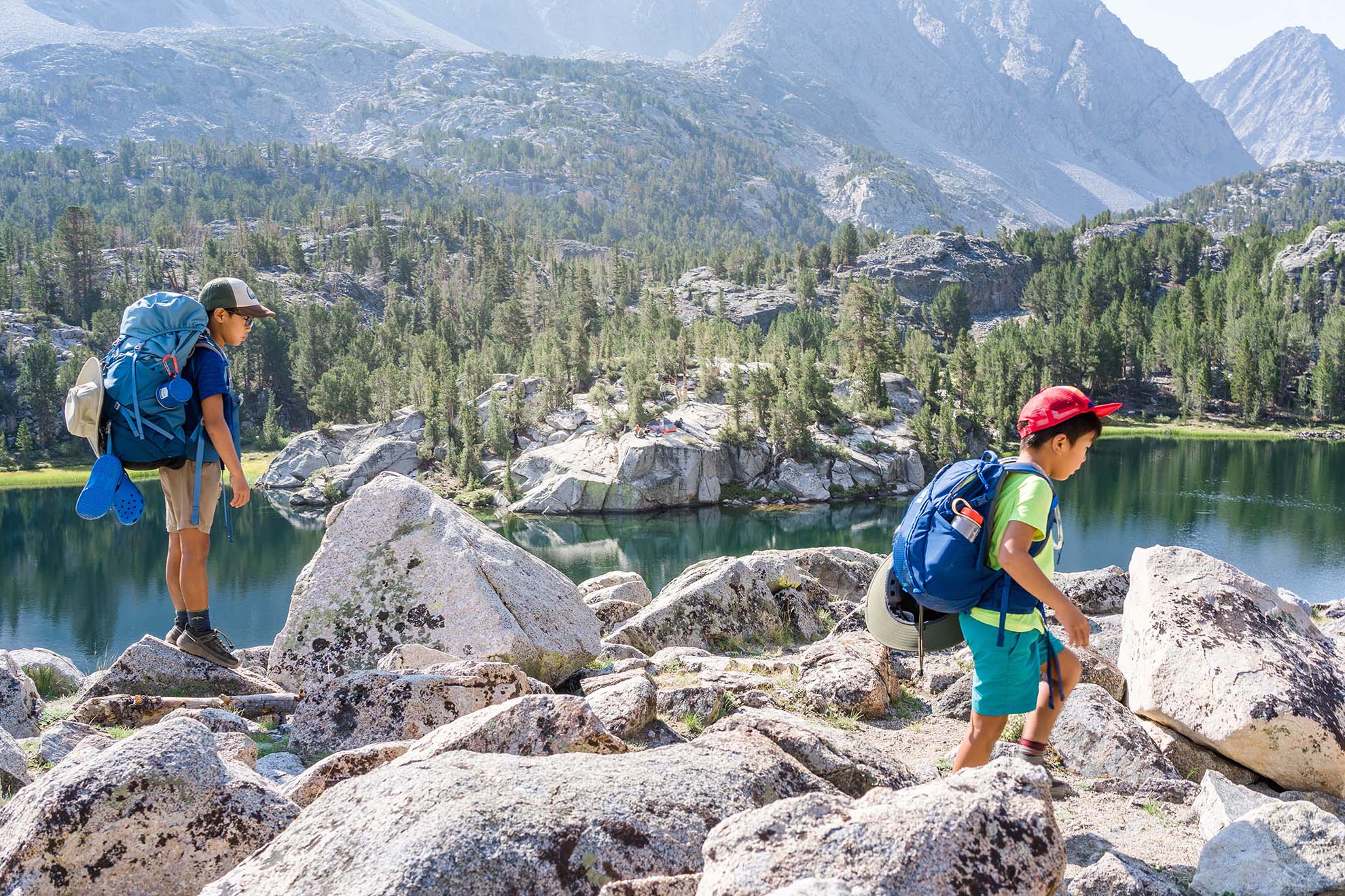 Two boys backpacking on rocks with lake in background