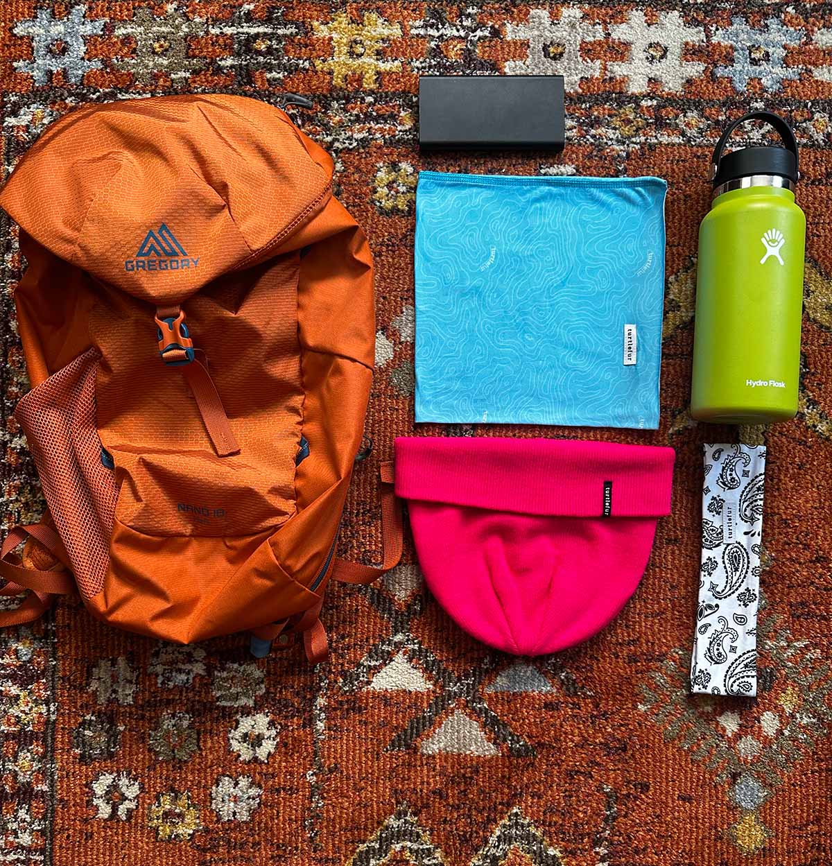 flatlay image of backpack, neck gaiter, hat, water bottle, gear