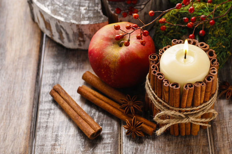 a decorated candle next to cinnamon sticks and an apple