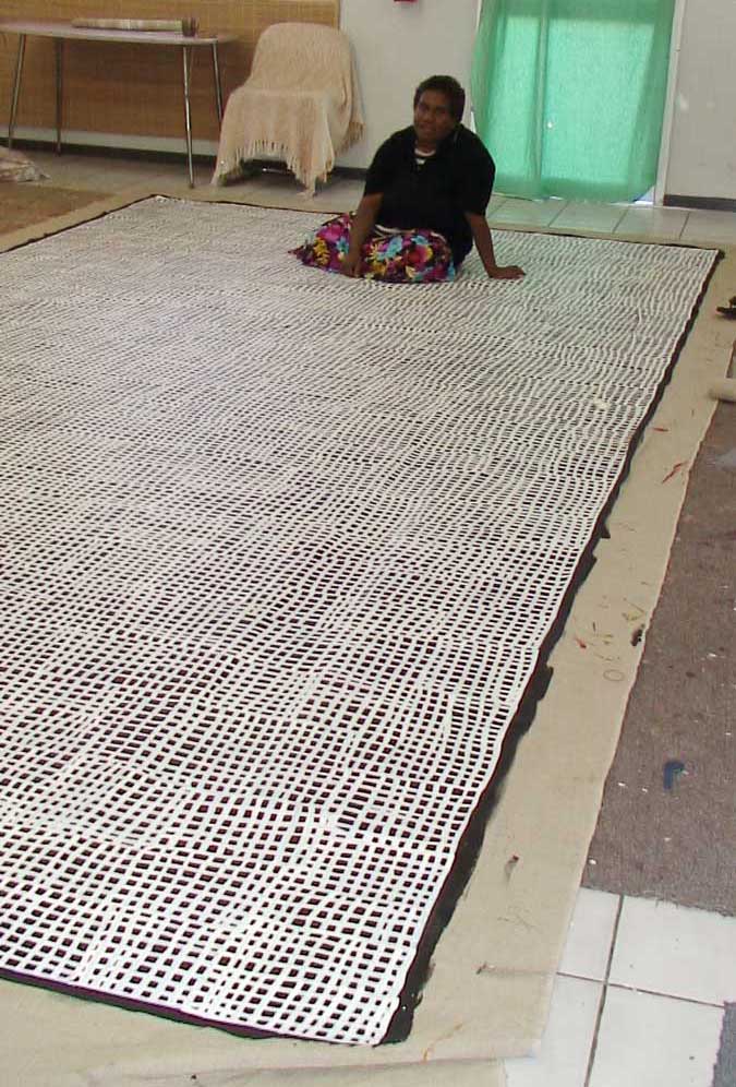 Abie Loy Kemarre sitting on top of large painting in studio