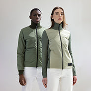 Man and woman pose against a grey background. Man on left wears the Layton Men's Tactical Hybrid Sweater in Clover. Woman on right wears the Evo Ladies Performance Full Zip Sweater in Clover.