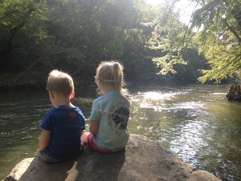 Two small children sitting on a rock beside a river