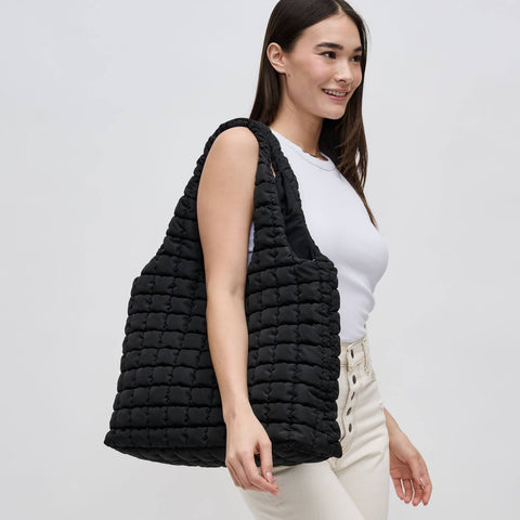 a model in a white top carrying a black quilted tote bag