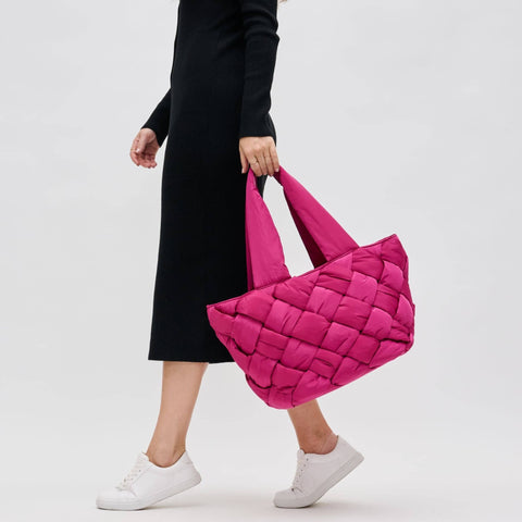 a model in black carrying a bright pink puffer tote bag