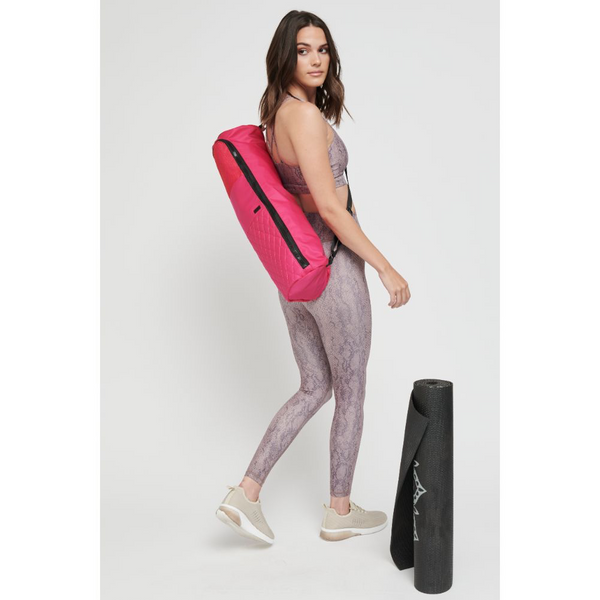 a model in patterned leggings carrying a pink yoga mat bag