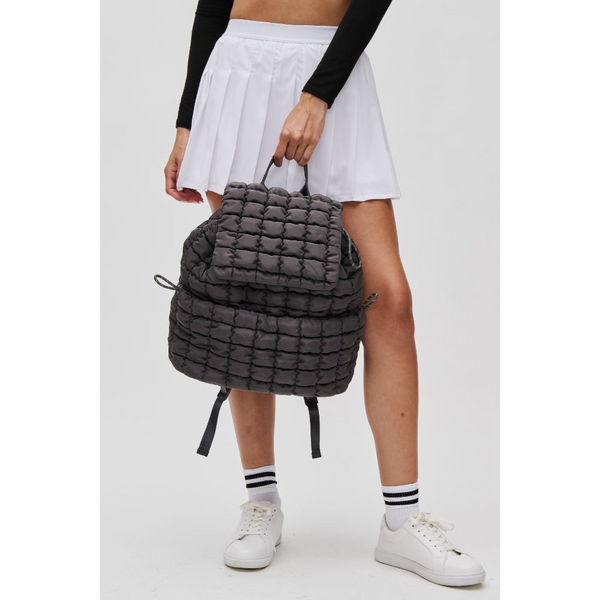 a model in a white skirt holding a black puffer-style backpack