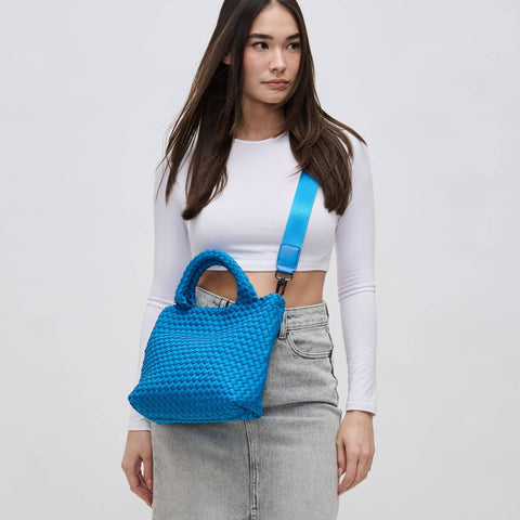 a model in a white top wearing a bright blue woven crossbody bag