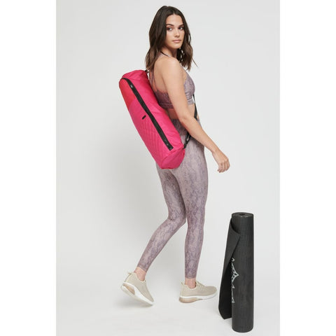 a model carrying a bright pink yoga mat bag with a black yoga mat beside her