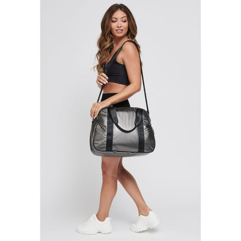 a model carrying a gray duffel bag made from a high-shine, metallic fabric