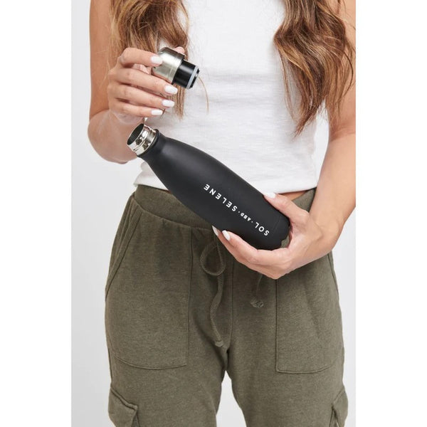 woman holding a black metal water bottle with the lid removed 