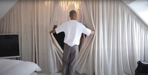 Ein Mann öffnet einen großen beigen Vorhang im Schlafzimmer und enthüllt einen Kleiderschrank dahinter