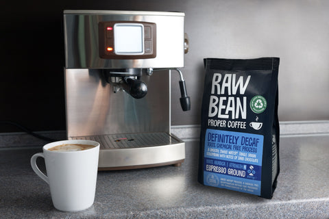 A pack of Raw Bean Espresso Ground coffee with an espresso machine and latte