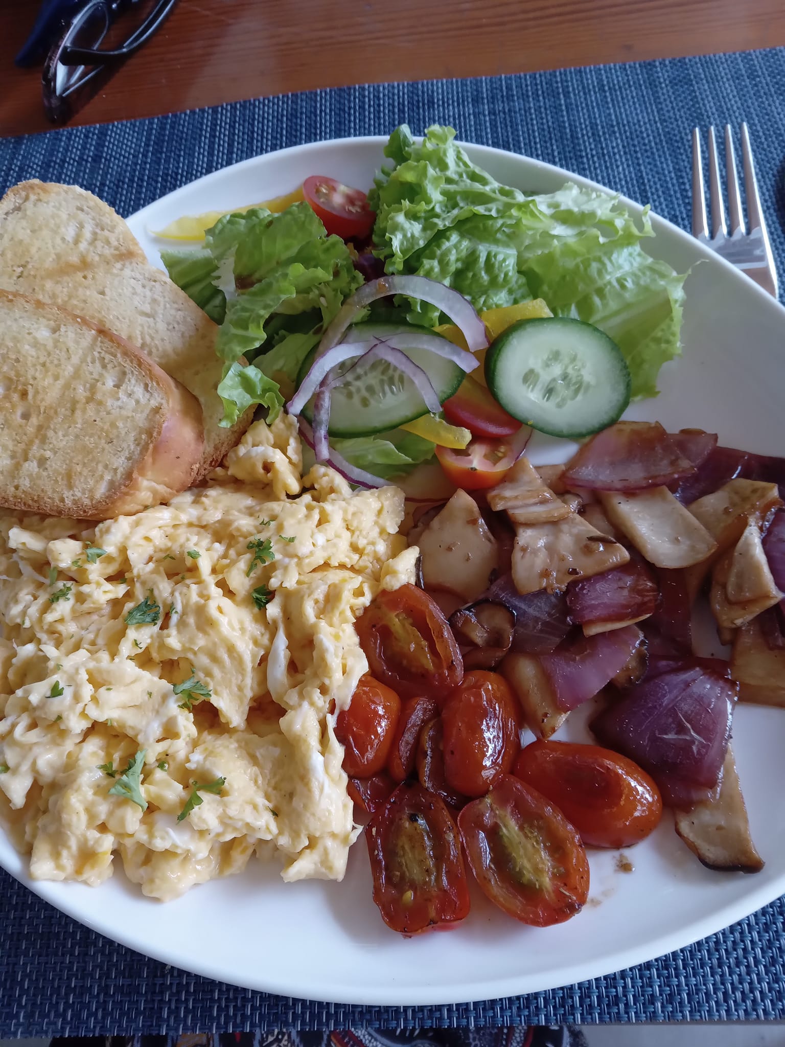 A plate of North American style breakfast of scrambled eggs, tomatoes, green salad and toast