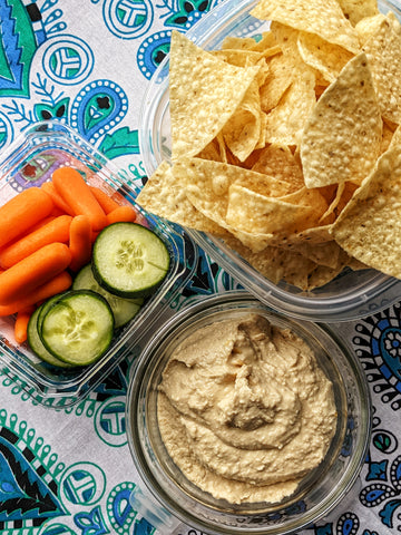 A beach blanket with tortilla chips, cucumber, carrot & hummus ready for beach snacking