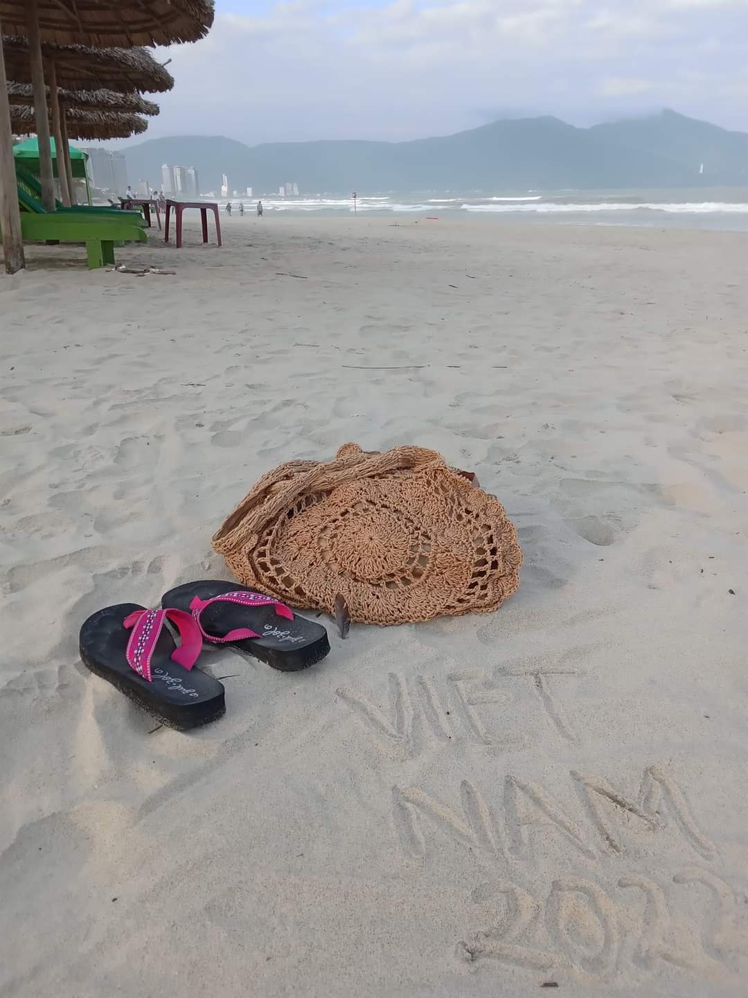Woven purse and flip flops on the sand of the beach in Da Nang, Vietnam